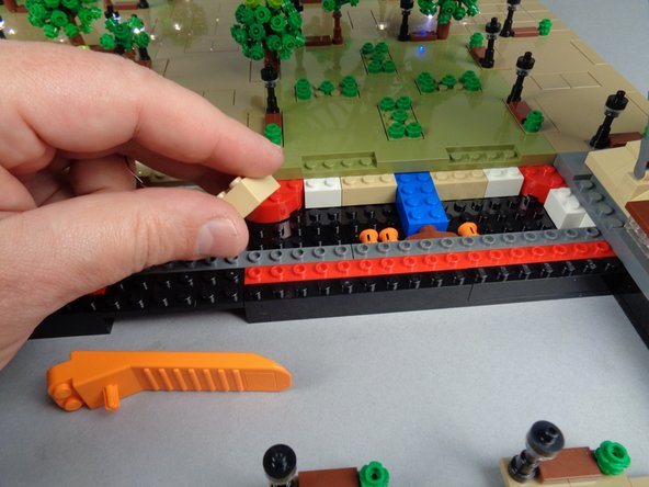 As shown in the second and third photos for this step, remove the 2x3 tan brick under Panel 4F and run the control cable between the studs on the black bottom plate, then re-attach the tan brick on top of the cable.