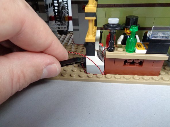 As shown in the first and second photos for this step, secure the lamp LED light wire with the same large black tile you used to secure the fireplace wire.