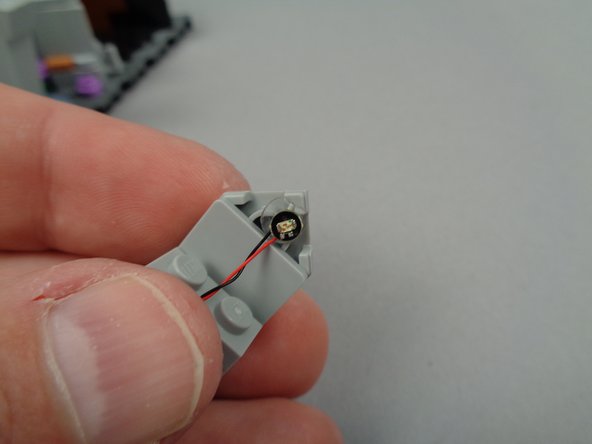 As shown in the first photo for this step, remove the back of the sticky dot and stick the first yellow light to the top of the backside of the tombstone.  Make sure the light is mounted with its wire passing downward.