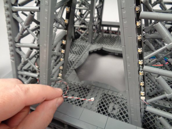 As shown in the first two photos for this step, pass the control cable connected to the fourth adapter board through the center of the fourth pillar and back toward the first pillar.