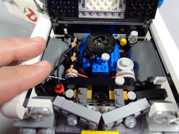 As shown by the orange arrows in the third photo, pass the wire under the engine hoses toward the front of the Ecto-1.