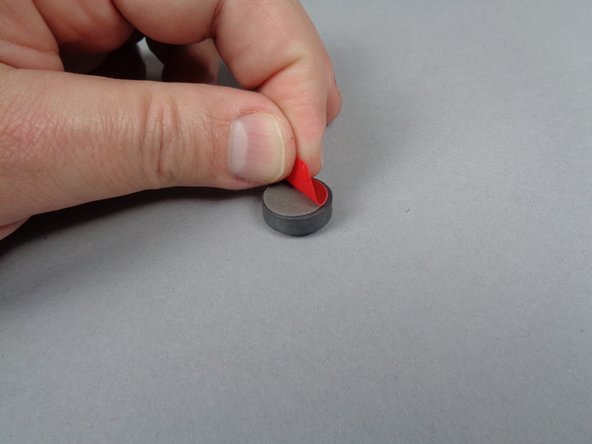 As shown in the photos for this step, remove the adhesive from the back of the magnet, and stick it to the center of the elevator between the two yellow LEGO brackets.