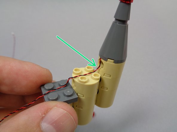 As shown in the first photo by the green arrow, make sure the light wire runs down along the side of the topmost tower with a little extra slack.  Also make sure the wires pass BETWEEN the studs on the round piece below.