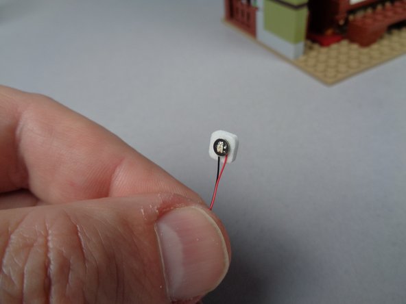 As shown in the first photo for this step, attach a sticky square to the back of the Pico LED light with the black base-- this is the red LED light.