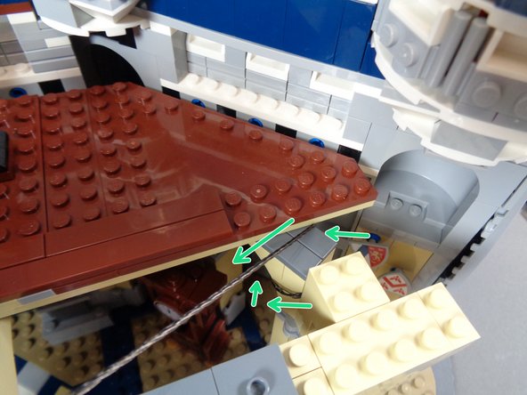 As shown by the green arrows in the second photo, wrap the two black wires once around the tan pillar under the brown floor pieces, being careful to wrap the wires over the dark bluish gray tile and not over any studs.