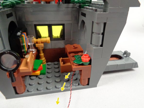 As shown by the yellow arrows  in the first and second photos for this step, pass the LED light wire through the open wall, underneath Jack's desk and out the back side of the house.