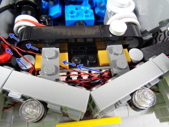 Carefully re-attach the grille assembly.  As shown by the blue arrows in the first photo for this step, pass the wires for the two hood strobe lights toward the left side.