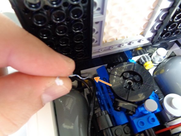 As shown by the orange arrow in the second photo for this step, pass the wire through the hole and pull it out from the other side, in the area under the hood by the engine.