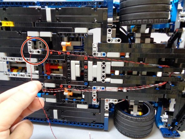 As shown in the second photo, route the wire toward the rear of the car, looping it up and through the pin hole in the Technic bracket as shown by the red circle.