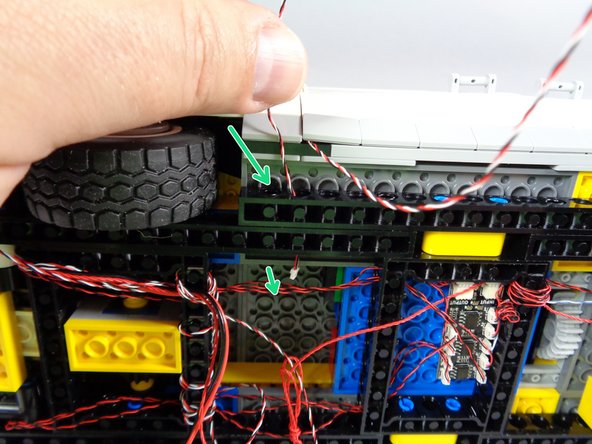 As shown by the green arrows in the first photo for this step, pass the wire for the door switch through the holes in the black Technic frame.
