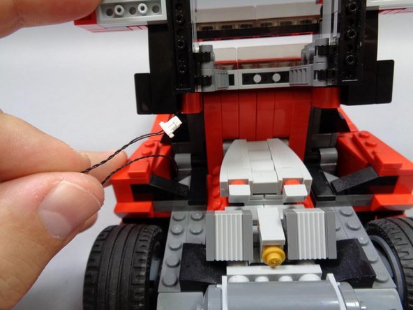 As shown in the second and third photos, take the black connecting cable you ran from the front of the car in Steps 15-16, pull it up from the bottom of the car into the space under the rear hatch, and secure the cable with the light gray 1x3 plate.
