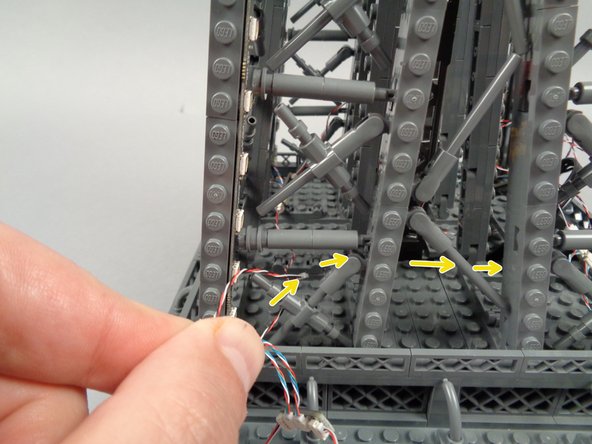 As shown by the yellow arrows in the second photo for this step, pass the control cable through into the center of the tower, and back toward the inter-level connecting board where your loop began.