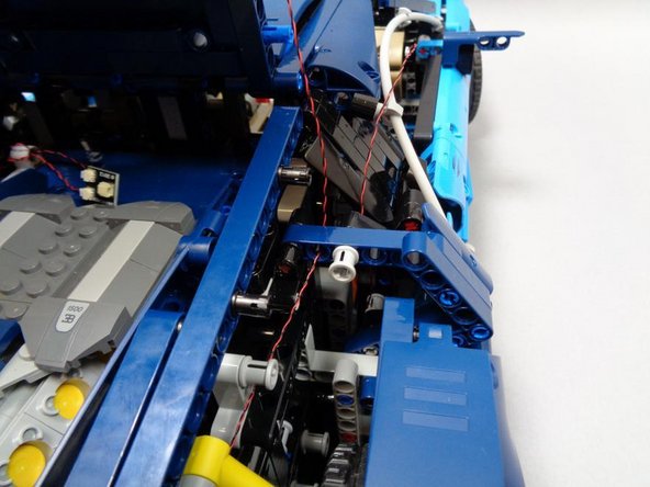 As shown in the first photo, continue routing the wire from the previous step through the hole in the blue Technic beam.