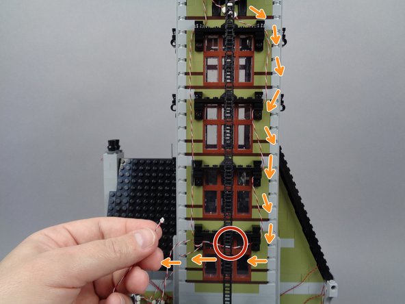 Once you have reached the fourth window down from the top of the tower as shown in the first photo for this step, you will need to cross the light strip wire to the opposite side of the tower as shown by the orange arrows.
