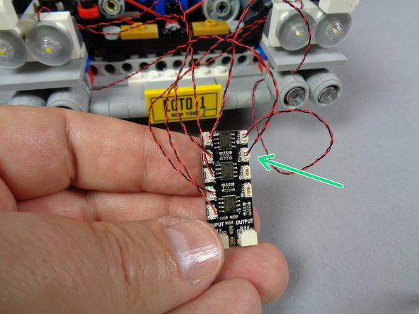 As shown in the first photo for this step, re-attach the third lower headlight with the light wire passing to the top and toward the center of the Ecto-1.