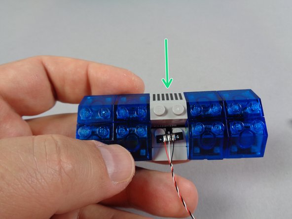 As shown by the green arrow in the second photo for this step, attach one of the top 2x2 slopes with printed lines on the side opposite the &quot;T&quot; shaped part.