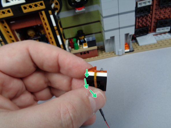 As shown by the green arrows in the first photo for this step, carefully bend the flexible wire back and underneath the 2x2 black LEGO plate that serves as the base for the fireplace.
