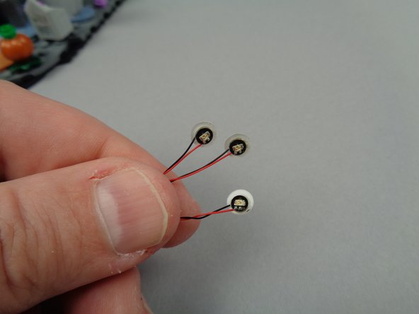 As shown in the photos for this step, remove the sheet of small sticky dots from the small Sticky Dots/Squares bag (provided inside Bag 1), and attach one dot each to the back side of the yellow LED lights.