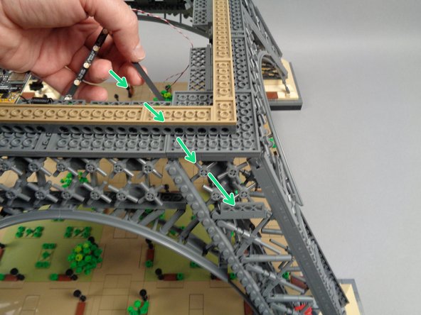 Use your tweezers to remove the backs of the sticky dots on the next two light strips, and carefully pass the ends of both strips down into the center of the structure as shown by the green arrow in the first photo for this step.