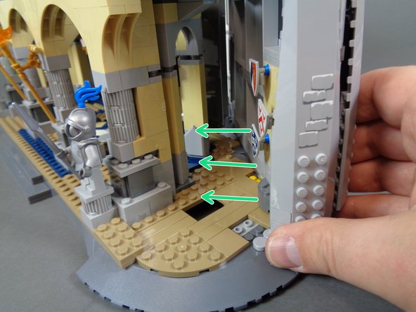As shown by the green arrows in the first photo for this step, carefully slide the outer castle wall back into place.