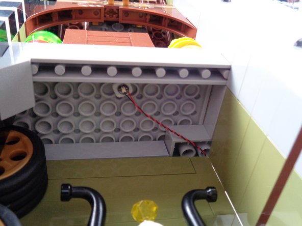 As shown by the purple arrows in the second photo for this step, pass the plug through the gap in the back wall, and pull the wire all the way through so the wire is tight as shown in the third photo.