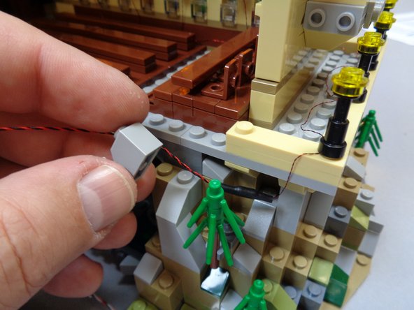 The photos in this step show one way to clean up the long wire connected to the nine street lamps.  The red circle in the third photo shows a 1x1 light bluish gray slope part that was taken from elsewhere on the castle's base and used to hold the light wire in place.