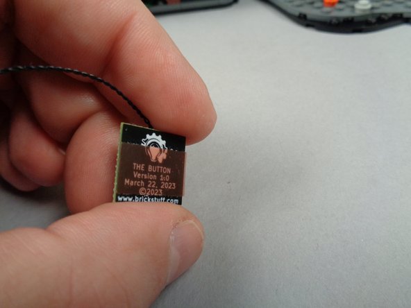 As shown in the first photo for this step, the large button has permanent adhesive tape (visible as red) on the back side.  You can use this to mount the button in a location of your choosing (the second photo shows one potential mounting spot).