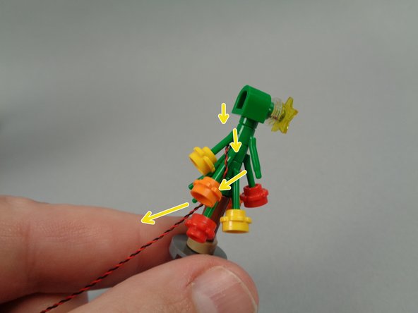 As shown by the yellow arrows in the second photo for this step, route the light wire down through the tree, using the flower plates on the branches to help hold the wire in place.