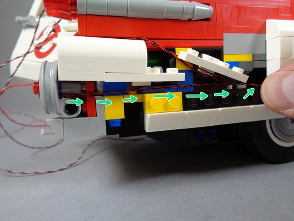 As shown by the green arrows in the first photo for this step, route the wire for the tail light along the side of the vehicle frame, and into the interior through the side, as you did for the other two tail light wires.