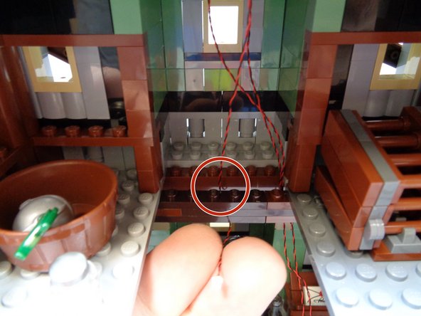As shown in the second photo, pass the green light wire down through the hole in the attic floor, making sure to pass the wire BEHIND the horizontal floor support as shown by the red circle.
