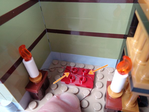 As shown by the arrows in the second photo for this step, pass the first candle wire between the studs underneath the obelisk, not on top of the studs.