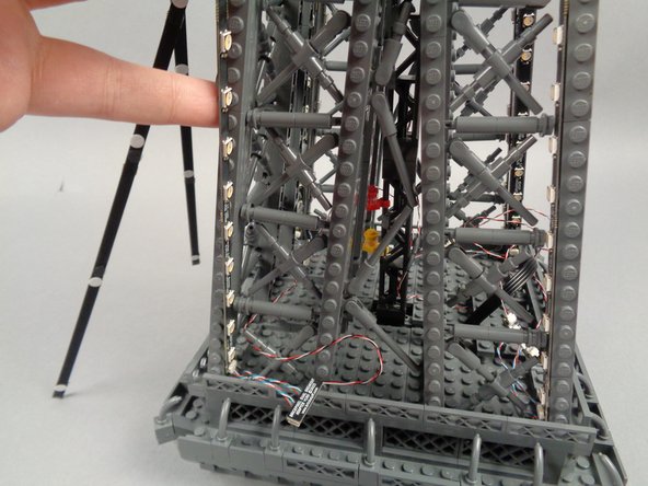 Remove the backs of the sticky dots on the second light strip (connected to plug #2 of the adapter board), and attach the strip to the tower frame as shown in the photos for this step.