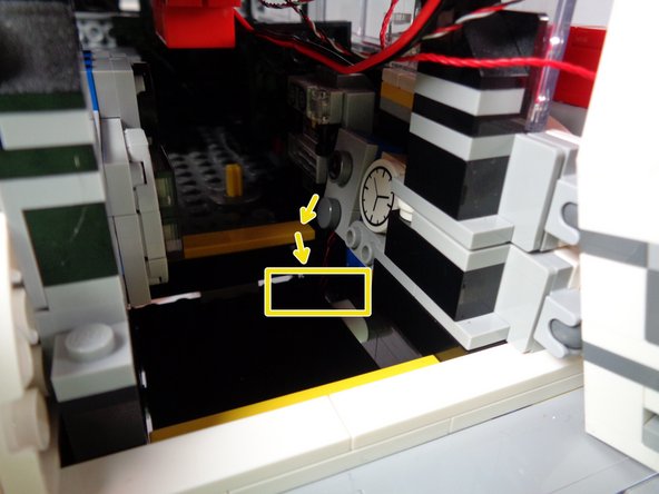 As shown by the yellow arrows and yellow rectangle in the first photo for this step, carefully feed both tail light wires down underneath the vehicle by passing the wires behind the hinge for the rear platform.