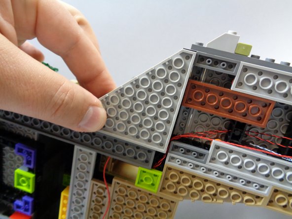 As shown in the third photo, carefully re-attach the large triangle shaped plate.  As you re-attach the plate, make sure the red wire passes between the studs of the plate, and not on top or over any studs.