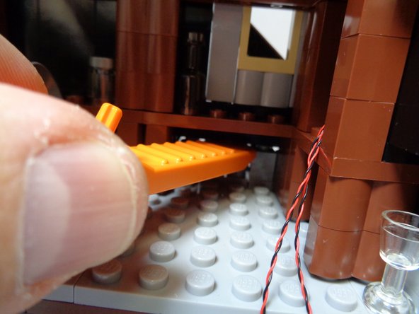 As shown in the first photo, use a brick separator to pry up the roof section and remove one of the round 1x1 LEGO® bricks as shown in the second photo.