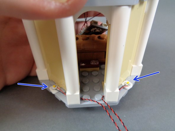 As shown by the two blue arrows in the third photo, use two small sticky squares to attach the lights to the front of the tower floor.  Carefully replace the two white columns, making sure the two LED light wires pass between, not on top of, any studs.
