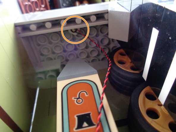 As shown by the orange circle in the third photo for this step, attach the second green LED light to the ceiling in the obelisk room, behind the long light bluish gray brick so the green light is hidden from view when looking directly at the open mansion.