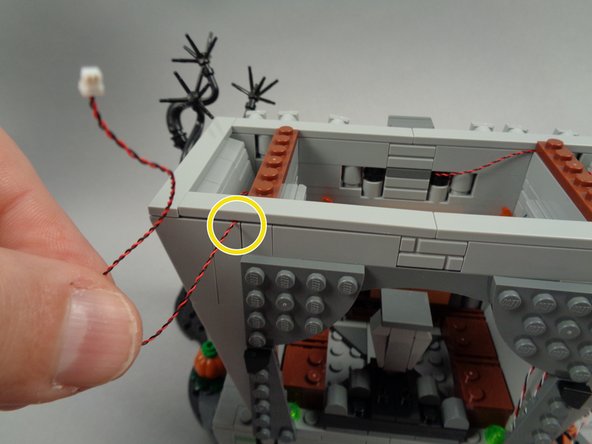 As shown by the circle in the second photo for this step, route the light wire for the left torch between studs, then re-attach the long tile to hold the wire in place.