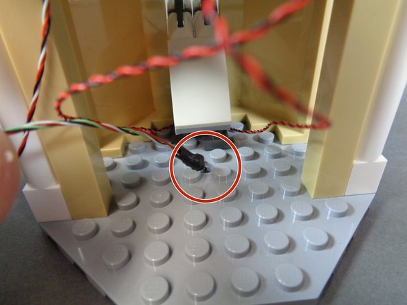 As shown in the second photo, pass the black connector through the hole in the floor, so the cable extends under the bottom of the floor as shown in the third photo.