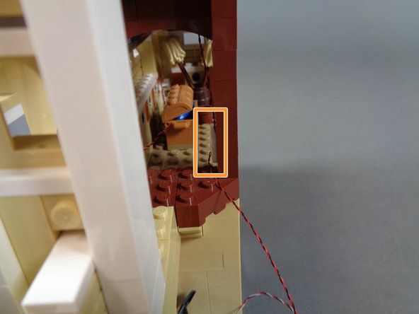 The orange rectangle in the second photo shows a side view with the large sticky square holding the light wire in place behind the brown pillar.