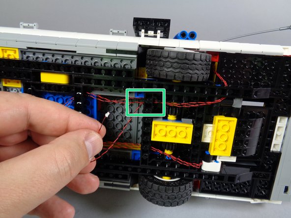 As shown by the green rectangles in the first and second photos for this step, continue passing the tail light wire through the holes in the black Technic frame until the wire reaches the area of the BRANCH09X adapter.