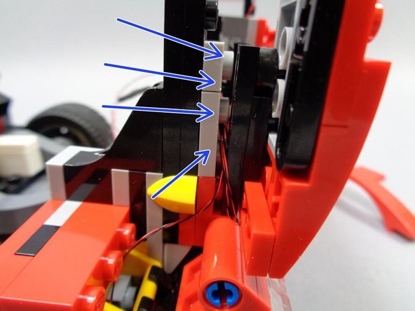 As shown by the blue arrows in the first photo, gently separate the plates under the hood so the headlight wires can run between one of the LEGO® studs.