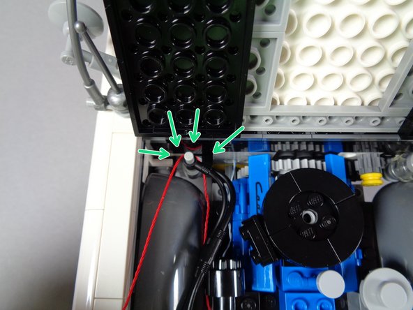 As shown by the green arrows in the first photo for this step, route the red wire behind and around the bar at the rear of the engine.  This provides strain relief for the wire.