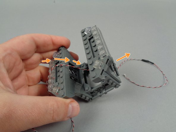 As shown by the orange arrows in the first photo for this step, pass the end of the flexible LED light strip wire down through the center of the broadcast tower.