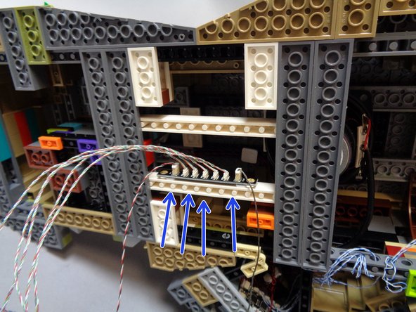 Now that you have the five spotlights connected to the BRANCH17 adapter board, use the sticky squares to mount the adapter along the long white brick under the castle, next to the speaker as shown in the first photo.