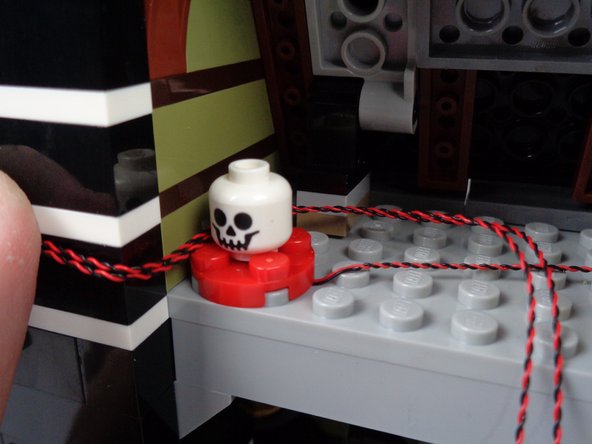 As shown in the second photo, it might help to remove the green jar cover while routing the wires.  The goal is to use the jar to help hold the two red LED light wires in place between the jar and the wall.