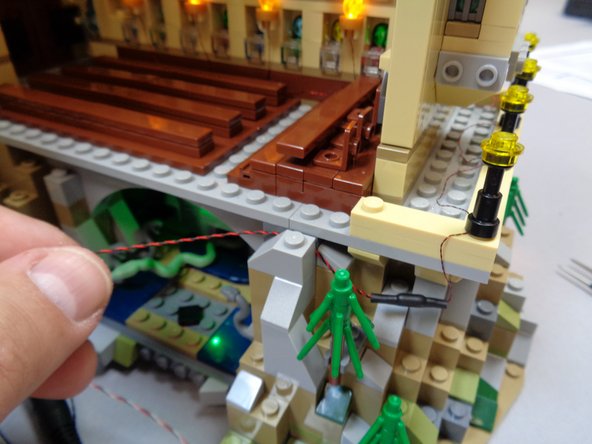 The photos in this step show one way to clean up the long wire connected to the nine street lamps.  The red circle in the third photo shows a 1x1 light bluish gray slope part that was taken from elsewhere on the castle's base and used to hold the light wire in place.