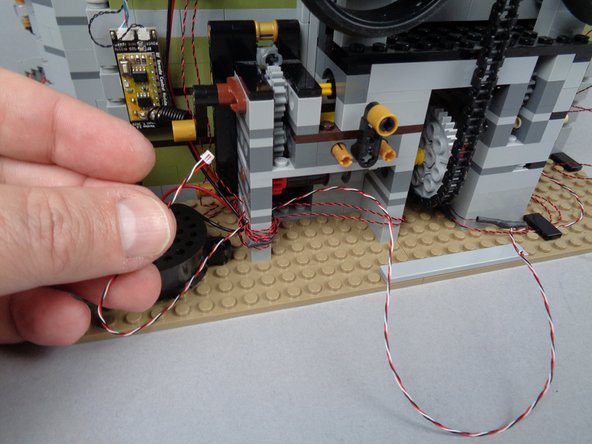 As shown in the first photo, you can lift and re-attach one of the 1x2 LEGO tiles to hold the wire down.  You can also use another of the 1x2 tiles in your LEGO parts bag.
