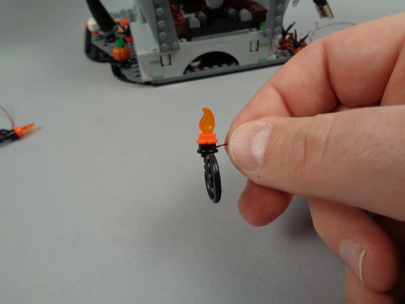 As shown in the two photos for this step, finish re-assembling the two torches by re-attaching the black whip pieces to the bottom of each.