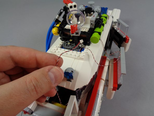 As shown in the first photo for this step, you should be able to pull the lightbar control wire fully out of the back of the Ecto-1, pulling the wire tight on the roof.